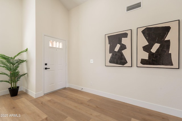 foyer entrance featuring a towering ceiling, baseboards, visible vents, and light wood-style floors