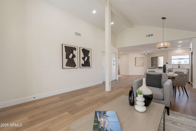 living area with visible vents, beam ceiling, light wood-type flooring, and high vaulted ceiling