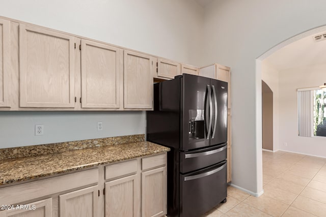 kitchen featuring light brown cabinetry, light stone countertops, light tile patterned flooring, and black fridge