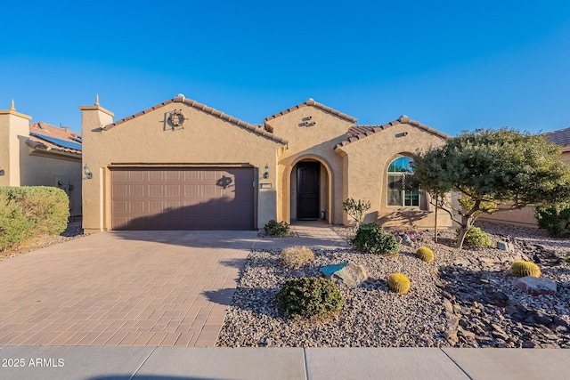 mediterranean / spanish-style house with stucco siding, a tile roof, decorative driveway, and a garage