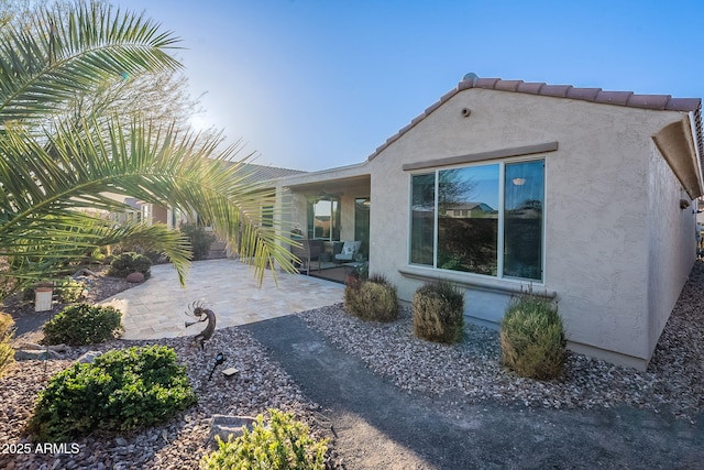 rear view of house with stucco siding, a tile roof, and a patio area