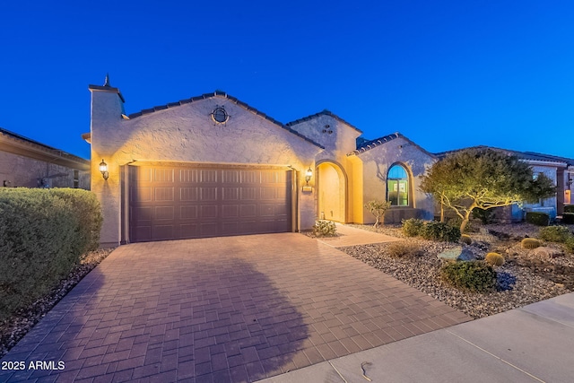 mediterranean / spanish home featuring decorative driveway, a garage, a chimney, and stucco siding