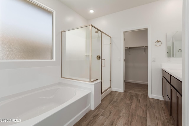 full bathroom featuring a walk in closet, a garden tub, wood finished floors, a shower stall, and vanity