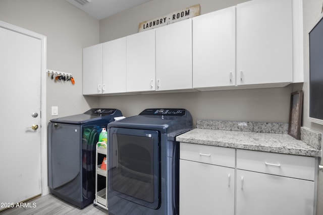 laundry room with cabinets, washing machine and dryer, and light wood-type flooring