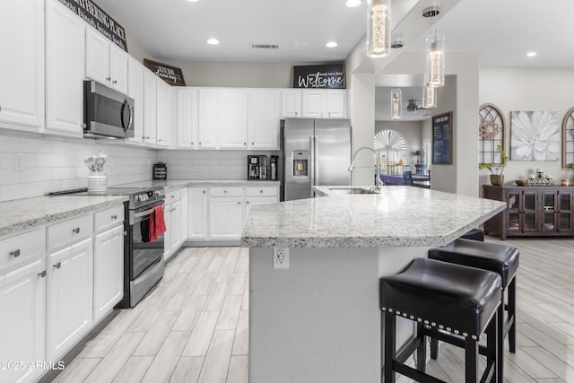 kitchen with white cabinets, appliances with stainless steel finishes, an island with sink, a kitchen breakfast bar, and sink