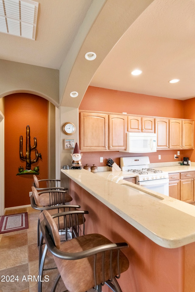 kitchen featuring light brown cabinets, a kitchen bar, white appliances, and light tile patterned floors