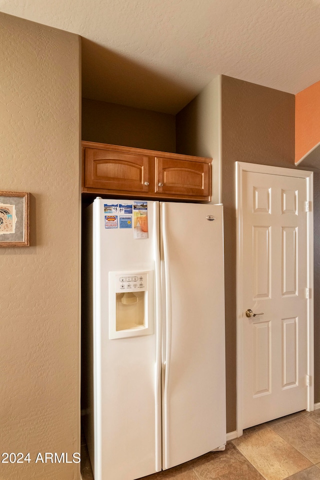 kitchen with a textured ceiling, white refrigerator with ice dispenser, and light tile patterned flooring