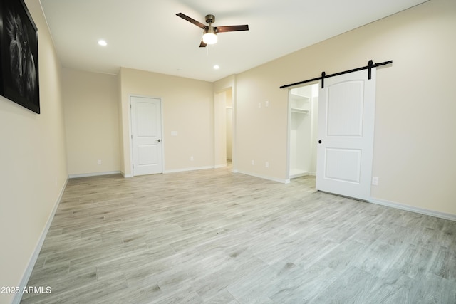 unfurnished room featuring ceiling fan, a barn door, and light hardwood / wood-style flooring