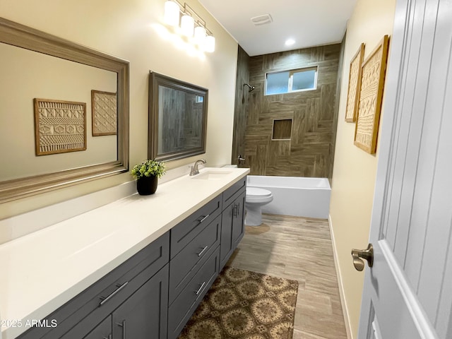 full bathroom with hardwood / wood-style flooring, tiled shower / bath combo, vanity, and toilet