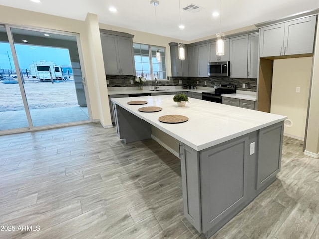 kitchen featuring gray cabinetry, black range with electric stovetop, decorative light fixtures, a center island, and sink