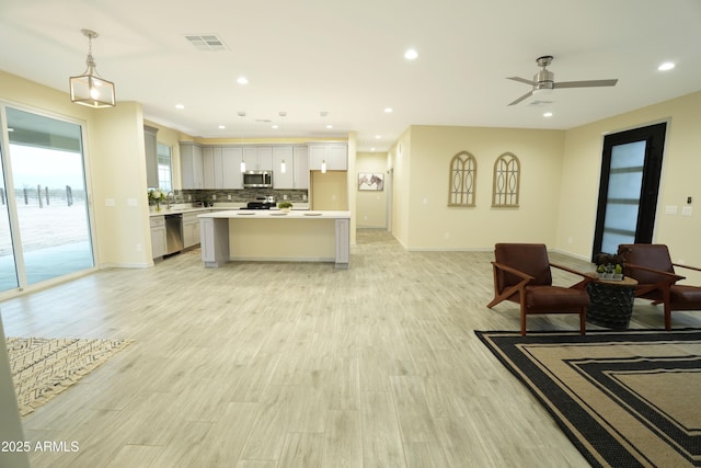 kitchen with appliances with stainless steel finishes, decorative light fixtures, light hardwood / wood-style floors, backsplash, and a kitchen island