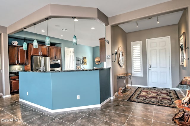 kitchen with hanging light fixtures, stainless steel appliances, dark stone counters, and kitchen peninsula