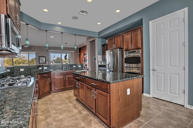 kitchen featuring a kitchen island, appliances with stainless steel finishes, sink, dark stone countertops, and hanging light fixtures