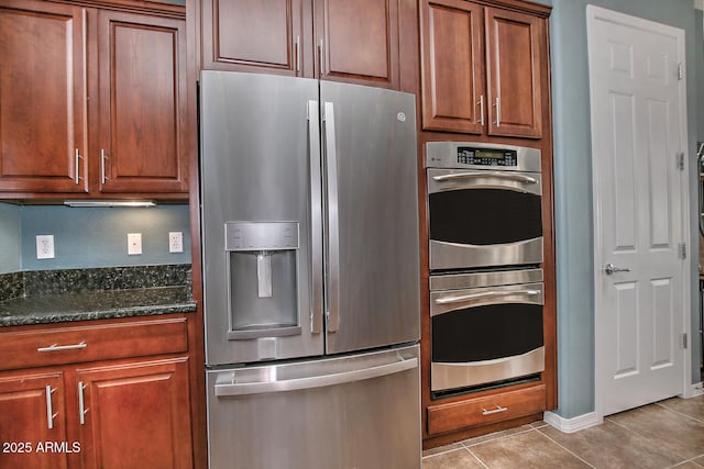 kitchen with stainless steel appliances, light tile patterned floors, and dark stone counters