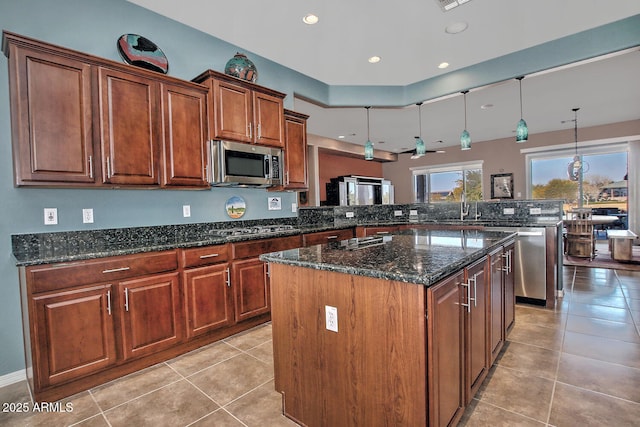 kitchen with a kitchen island, dark stone countertops, hanging light fixtures, kitchen peninsula, and stainless steel appliances