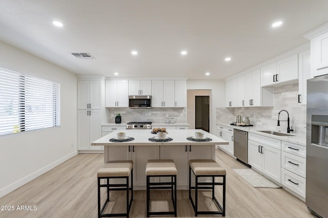 kitchen featuring appliances with stainless steel finishes, a kitchen island, white cabinetry, sink, and light hardwood / wood-style flooring