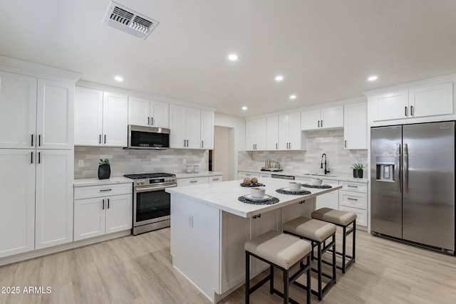 kitchen featuring stainless steel appliances, a center island, a kitchen breakfast bar, white cabinets, and sink