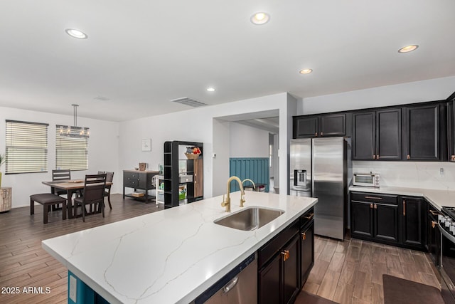 kitchen with sink, appliances with stainless steel finishes, dark hardwood / wood-style floors, a center island with sink, and decorative light fixtures