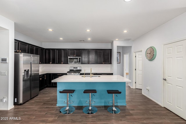 kitchen with appliances with stainless steel finishes, sink, a kitchen bar, decorative backsplash, and a kitchen island with sink