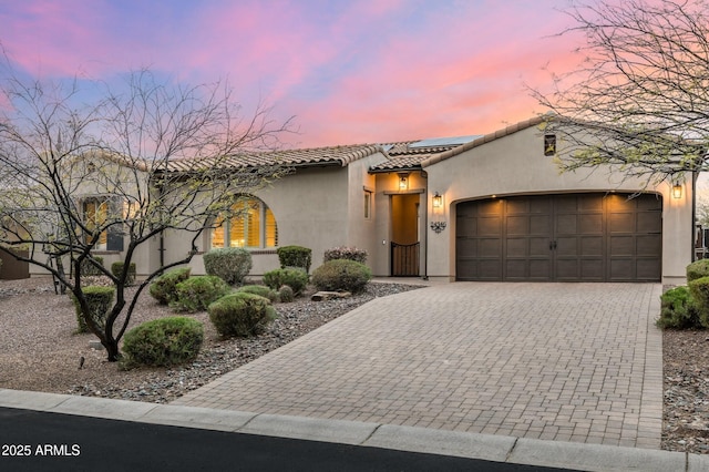 mediterranean / spanish house with an attached garage, stucco siding, a tile roof, decorative driveway, and roof mounted solar panels