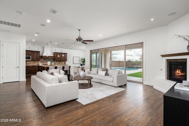 living room with a ceiling fan, visible vents, and dark wood-style flooring