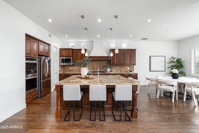 kitchen with decorative backsplash, premium range hood, dark wood-style flooring, and stainless steel appliances