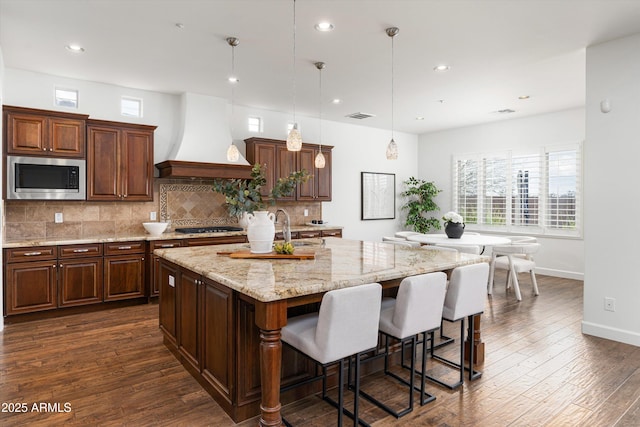 kitchen featuring stainless steel microwave, dark wood-style floors, visible vents, and premium range hood