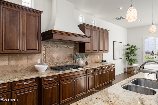 kitchen featuring visible vents, custom exhaust hood, a sink, stainless steel gas stovetop, and pendant lighting