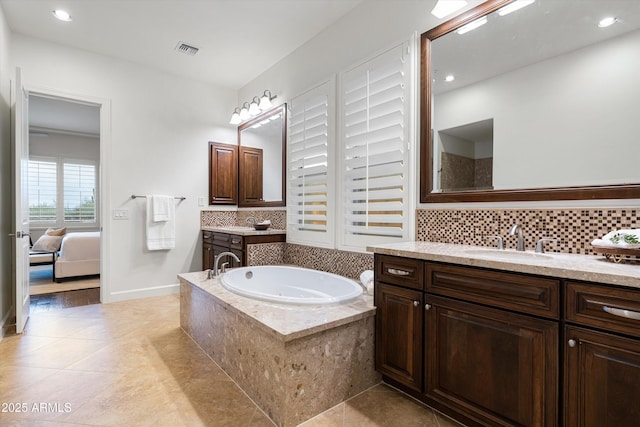 ensuite bathroom featuring visible vents, a garden tub, decorative backsplash, and a sink