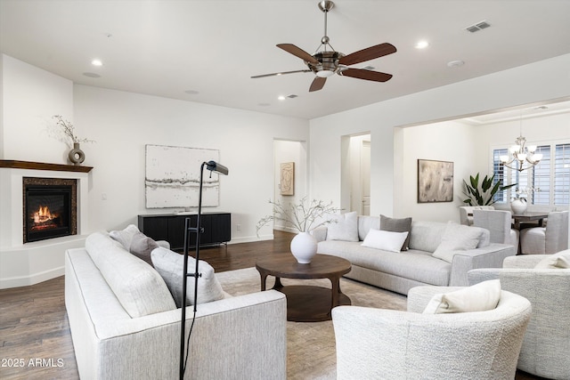 living area featuring a glass covered fireplace, wood finished floors, ceiling fan with notable chandelier, and visible vents