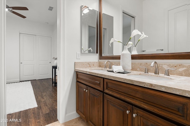 bathroom with wood finished floors, a ceiling fan, visible vents, double vanity, and a sink