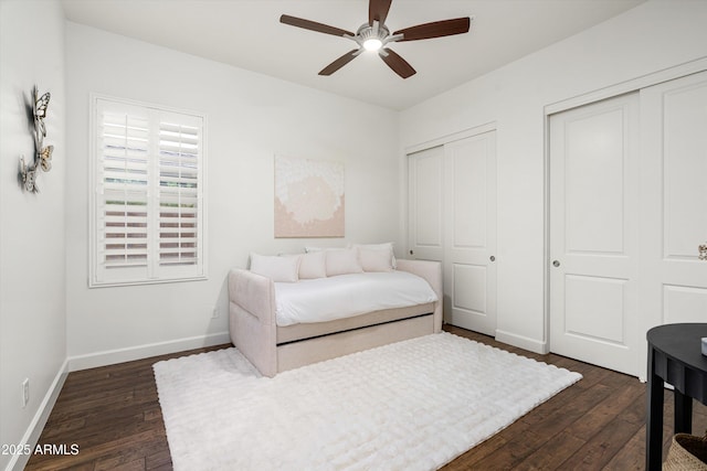 bedroom with dark wood finished floors, ceiling fan, two closets, and baseboards