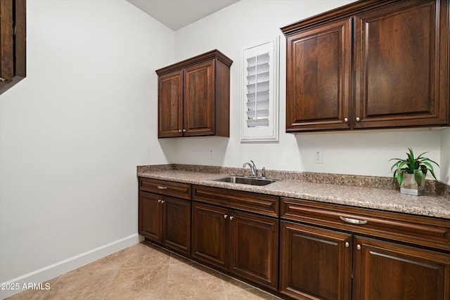 kitchen featuring light tile patterned floors, dark brown cabinets, baseboards, and a sink