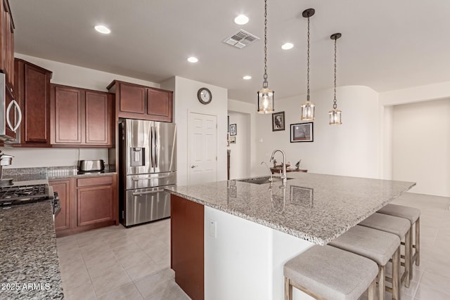 kitchen with light stone counters, a kitchen island with sink, sink, and appliances with stainless steel finishes