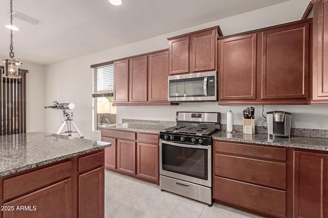 kitchen featuring dark stone countertops, light tile patterned floors, stainless steel appliances, and hanging light fixtures