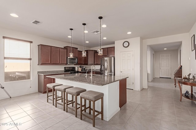 kitchen featuring sink, hanging light fixtures, stainless steel appliances, an island with sink, and dark stone counters