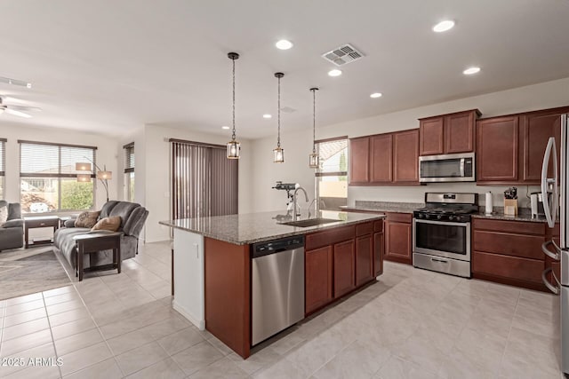 kitchen featuring sink, stainless steel appliances, dark stone counters, pendant lighting, and a center island with sink