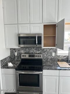 kitchen with white cabinets, appliances with stainless steel finishes, backsplash, and dark stone counters