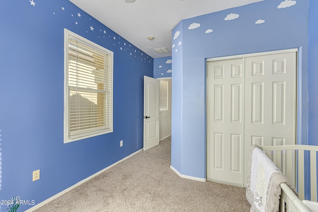 unfurnished bedroom featuring a crib, light carpet, and a closet