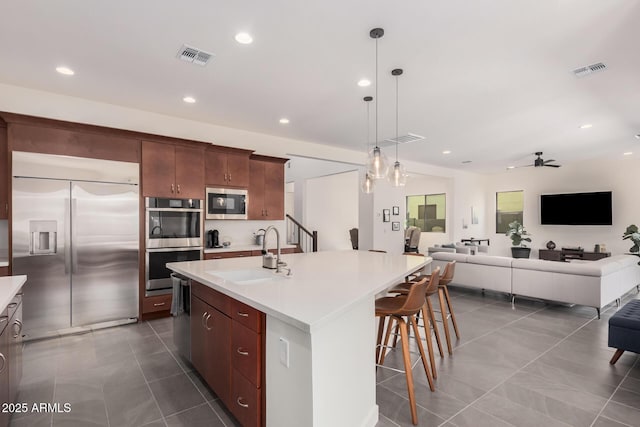 kitchen with sink, built in appliances, an island with sink, pendant lighting, and tile patterned flooring