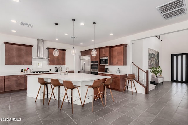 kitchen featuring a breakfast bar, stainless steel appliances, a center island with sink, decorative light fixtures, and wall chimney exhaust hood