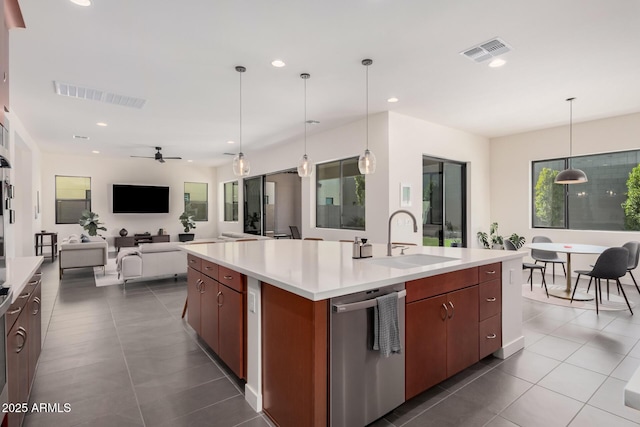 kitchen featuring sink, a center island with sink, stainless steel dishwasher, dark tile patterned flooring, and pendant lighting