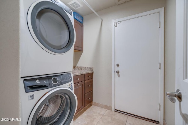 laundry room featuring cabinets, stacked washer / drying machine, and light tile patterned floors