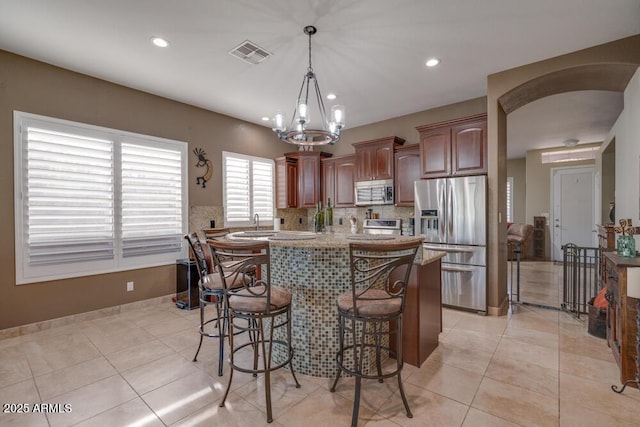 kitchen featuring light tile patterned flooring, a kitchen bar, decorative light fixtures, appliances with stainless steel finishes, and decorative backsplash