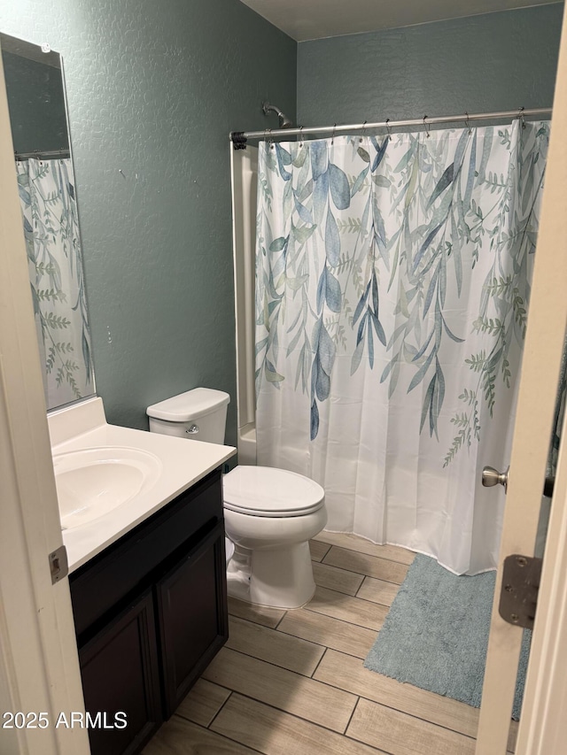 full bath with wood finish floors, toilet, shower / bath combo with shower curtain, a textured wall, and vanity