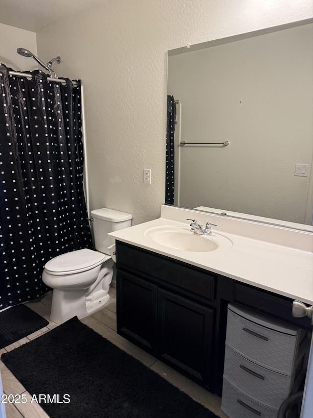 bathroom featuring toilet, vanity, a shower with shower curtain, and a textured wall