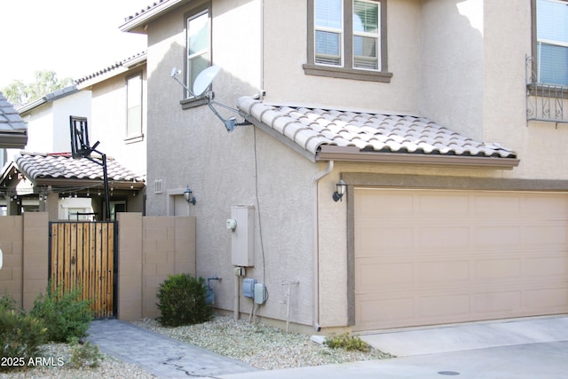 view of side of property featuring stucco siding, fence, a garage, and a tile roof