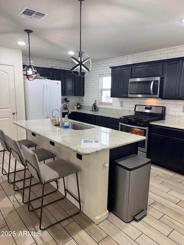 kitchen featuring sink, a breakfast bar area, pendant lighting, stainless steel appliances, and a kitchen island with sink