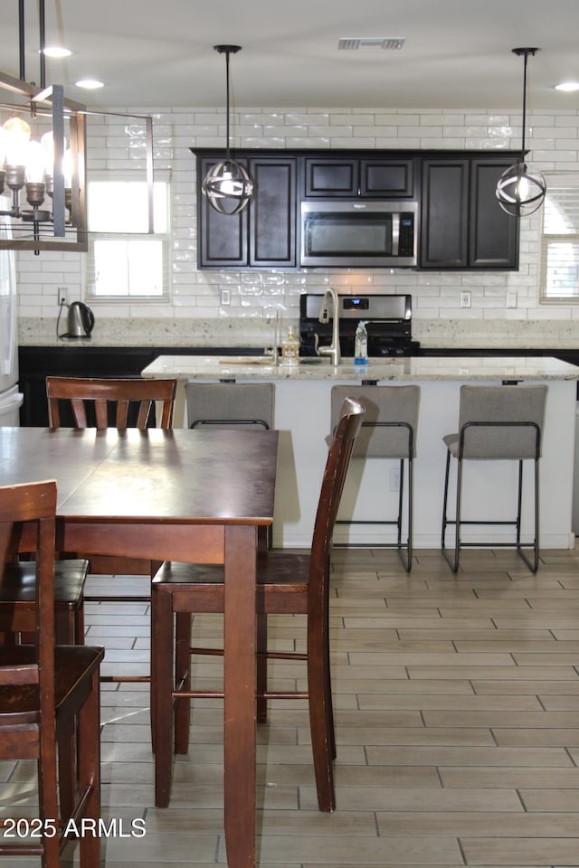 kitchen with decorative backsplash, hanging light fixtures, visible vents, and stainless steel appliances