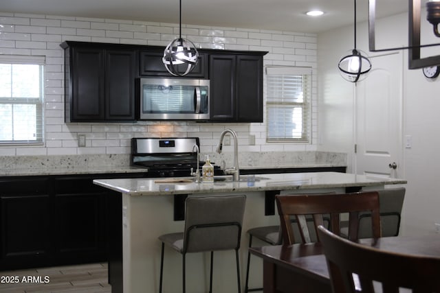 kitchen with a breakfast bar area, light stone counters, an island with sink, appliances with stainless steel finishes, and backsplash